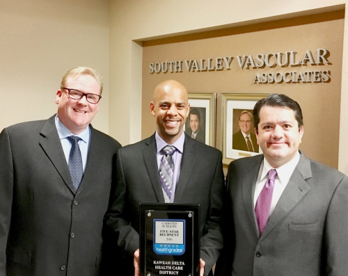 3 men smiling. man in middle holding award